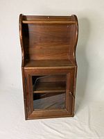 Full front view of the solid wood hanging vanity cabinet showing the curved top design and the closed glass door revealing the internal shelf.