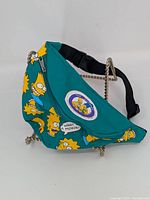 Front and side view of the green Simpsons fanny pack showing characters and patch, with chain and strap visible.