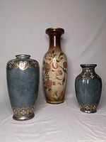 Three ceramic vases against gray backdrop, two blue-gray with gold floral accents and one tall beige vase with hand painted floral design, showing variety and size differences