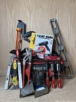 Front view of tool collection showing scraper, pliers, chisels, level, heat gun packaging and drll bits next to Husky tool bag.