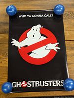 Front view of the Ghostbusters poster showing the logo, slogan, and colors with blue weights holding corners.