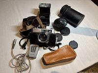 Top view of camera equipment lot showing Minolta Hi-Matic 7S camera, lenses, flash unit, shutter release cable and leather cases.