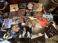 Photo showing collection of approximately 20 vinyl LP records spread on a table, including recognizable artists like Elvis Presley, Frank Sinatra, and Steve Miller. Various album covers in good pre-owned condition visible.