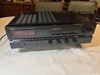 Front view showing full stereo receiver with display, function buttons, and control knobs on a table.