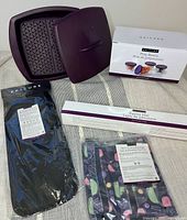 Overall view of the kitchenware bundle including boxed prep bowls, pastry mat, reusable bags in a veg print, skewers, and purple steamer parts.