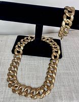 Gold tone chunky chain necklace laid flat and matching bracelet displayed on black velvet display stand