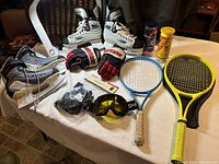 Full lot on table showing hockey skates, hockey gloves, tennis racquets, balls, goggles, and sports gear.