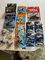 Full lot overview showing all items including Hot Wheels cars, Matchbox planes, Corgi plane, Tonka truck, and loose Maisto planes arranged on a table.