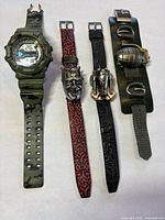 Four watches laid out on white surface showing camouflage digital watch, two Lucas Film character watches, and grenade face watch