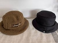 Photo showing two bucket hats: one brown sherpa fleece with bow detail and one black smooth fabric with Lululemon logo