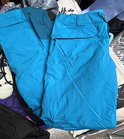 Full view of blue Marmot snow pants showing zipper pocket, closure, and logo.