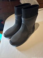Side angle view showing the right and left boots standing upright on a white surface highlighting ribbed rubber sides and neoprene upper.