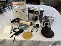 Overview photo showing the Timex clock radio, InstantMusic adapter in packaging, small speakers, and various cables and electronic devices arranged on a white table.