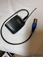 Sennheiser bodypack transmitter wireless unit with attached antenna and cable shown on a light-colored surface, displaying the connected cable and overall condition.