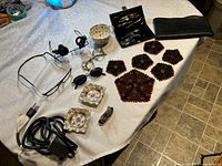 Photo showing vintage watchmaker glasses with black dual lenses, old spectacles, magnetic readers, beaded doily set, grooming kit in leather case, wallet, and china pieces arranged on a table.