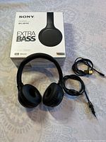 Sony WH-XB700 Extra Bass headphone box with headphones, USB charging cable and wired audio cable laid out on a patterned surface.