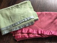 Two vintage wool blankets photographed together, one mint green and one coral, showing satin trims with some wear.