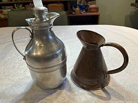 Both vintage items placed side by side on a white patterned tablecloth showing the thermos on the left and the copper jug on the right.