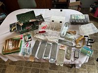 Top-down view of all vintage fishing tackle including multiple containers, spoons, lures, and other accessories spread on a white cloth.