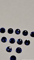 Photo showing thirteen round, faceted royal blue Ceylon sapphires arranged on a flat surface highlighting their color and clarity.