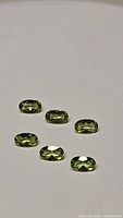 Six oval cut apple green peridot gemstones shown on white background. The stones are faceted with good brilliance.