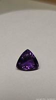 Close-up photo of a 6.77ct Brazilian amethyst trillion cut gemstone showing its deep purple color and clarity.