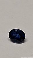 Oval cut royal blue sapphire gemstone on neutral background showing facets and color.