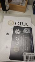 Photo showing loose round cut moissanite stone with GRA certification card and some background items.