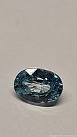 Close-up photo of an oval cut lagoon blue zircon gemstone showcasing its facets and color.