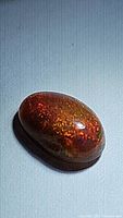 Close-up image showing the reddish tone and fiery play-of-color of the oval natural chocolate Ethiopian opal cabochon.