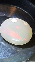 Close-up image of oval faceted Ethiopian opal with visible multicolored flashes primarily red and green.
