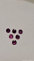 Six deep fuchsia and pink-purple round faceted rubies shown on a white background. The gems exhibit vibrant color and clarity.