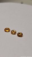 Three oval cut natural golden yellow sapphires arranged in a row on a white background showing rich golden color and clarity.