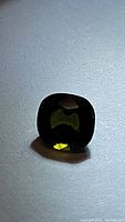 Photo showing the dark olive green cushion cut tourmaline gemstone from top down with light reflection highlighting facets.
