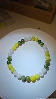 Clear photo of natural jade bead bracelet showing white, green, and lemon yellow beads arranged in a continuous circle under direct light