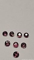 Seven round-cut, peach pink sapphires arranged on a white background, showing color, size, and facets.