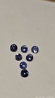 Seven round-cut natural tanzanite gemstones laid out, showing blue and purple hues with faceted reflections.