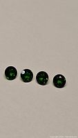 Four vivid green round cut calibrated Russian chrome diopside gemstones laid in row, showing their size and clarity