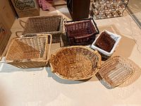 Seven wicker baskets arranged on floor showing variety of sizes, shapes and colors.