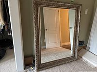 Full view of the large framed beveled mirror leaning against a wall in a carpeted room, showing the size and reflective surface.