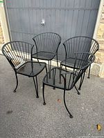 Set of four black metal outdoor chairs displayed outside on a driveway near a garage door