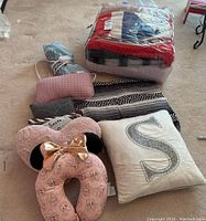Overall view of the blankets, cushions, and neck pillow arranged on carpet. Items include folded British Flag throw in plastic, blue heated blanket, patterned black and white rug, several cushions and the Minnie Mouse pink flight neck pillow.