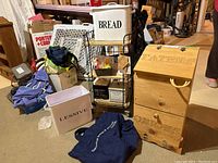 Overview of lot containing wood potato bin, metal storage bins including those labeled 'BREAD' and 'LESSIVE', and metal cart with wooden shelves on castors in basement setting