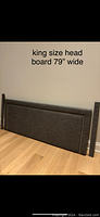 Photo showing dark grey king size headboard with silver studs and two wooden side supports on floor.