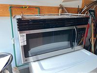 Over-the-range GE microwave oven showing the stainless steel front, black vent grills on top, glass door with handle on right side, control panel with buttons.