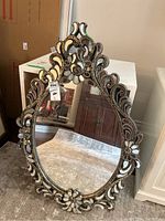 Full view of the ornate oval mirror showing intricate floral metal frame and reflective glass.