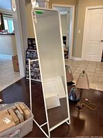 Tall white framed floor mirror standing upright with clothing rack base visible.