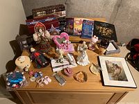 Overview of all items on wooden surface showing figurines, dolls, catalogues, and other collectibles