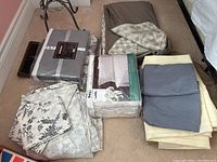 Overview of sheet sets and duvet covers spread on floor, showing various folded sheet sets and some packaged in plastic.