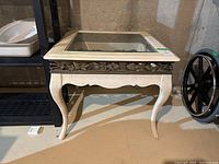 Full view of square wooden side table with beveled glass top and metal decorative border with floral design.